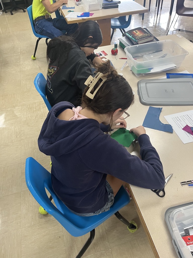 Two students are practicing sewing methods on a swatch of fabric.