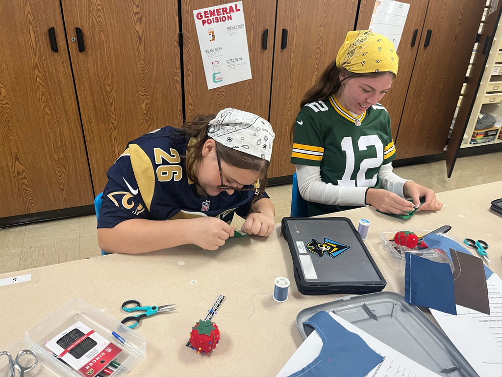 Two students are practicing sewing methods on a swatch of fabric.