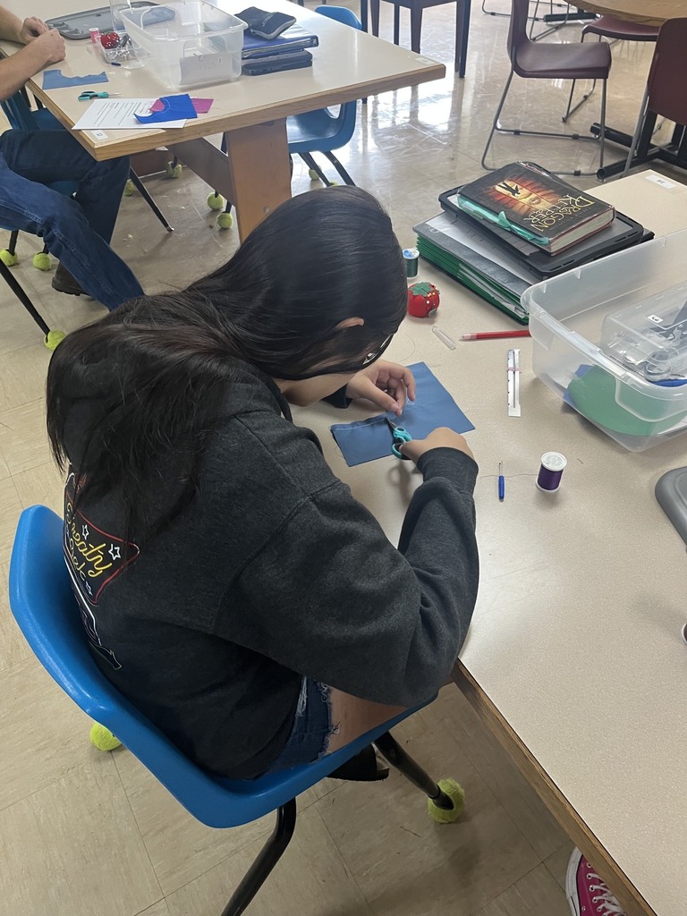 One student is practicing sewing methods on a swatch of fabric.