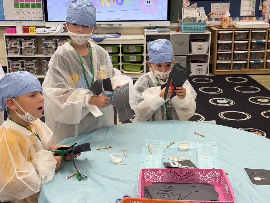 Three students are cutting black paper to make a skeleton.
