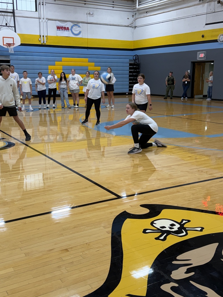 A team dressed in white is playing volleyball. One player has bumped the ball. 