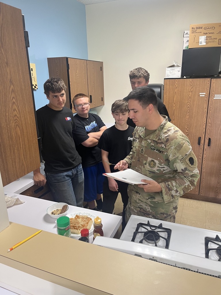 The soldier is trying a concocted meal. The cooks are watching.
