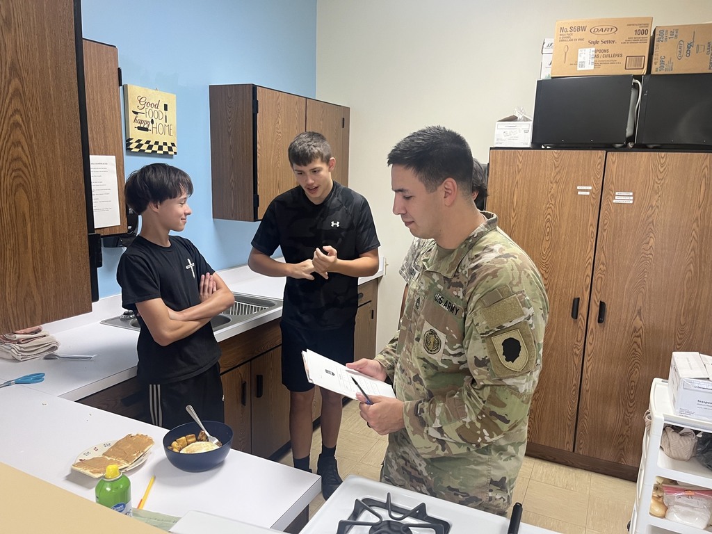 The soldier is trying a concocted meal. The cooks are watching.