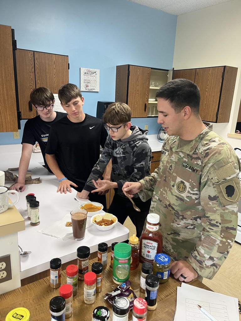 The soldier is trying a concocted meal. The cooks are watching.