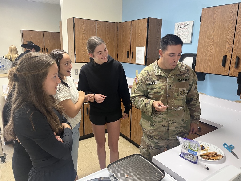 The soldier is trying a concocted meal. The cooks are watching.