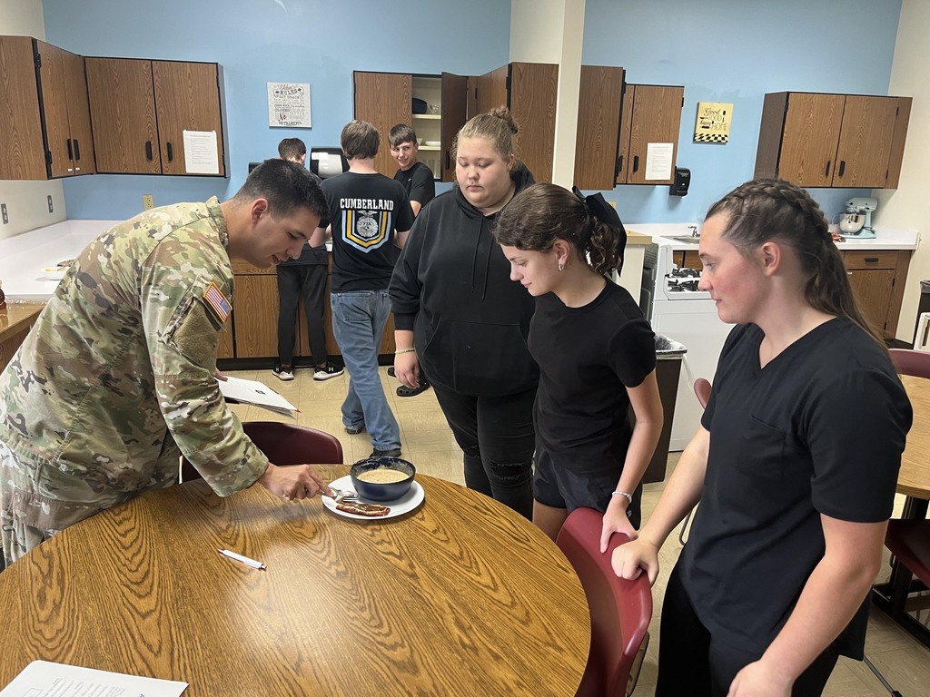 The soldier is trying a concocted meal. The cooks are watching.
