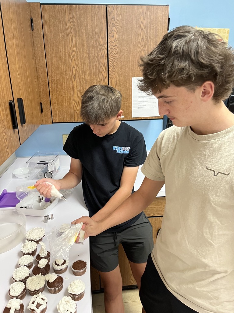 Two students are piping icing on cupcakes.