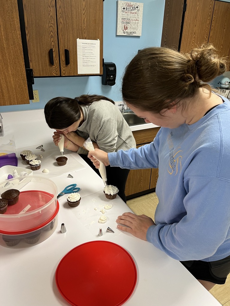 Two students are piping icing on cupcakes.