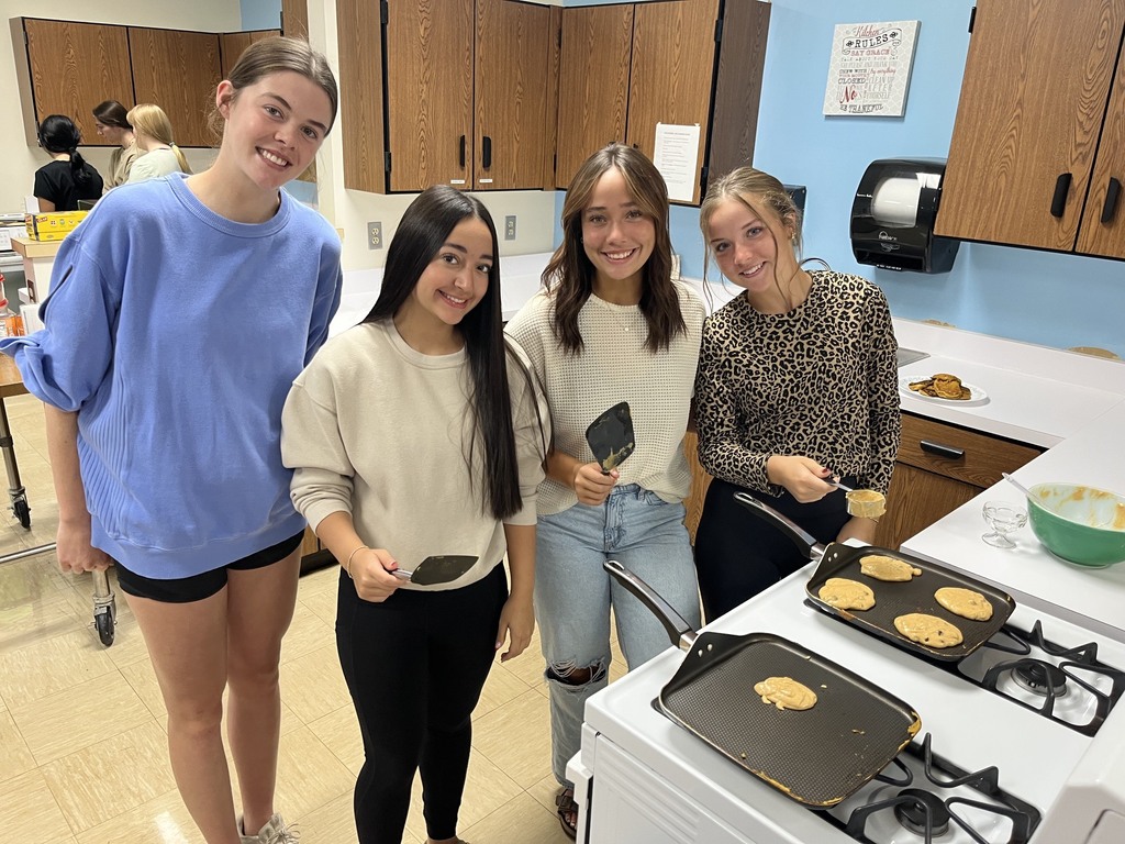 Four students are standing in front of the oven. Two have spatulas and there are two pans.