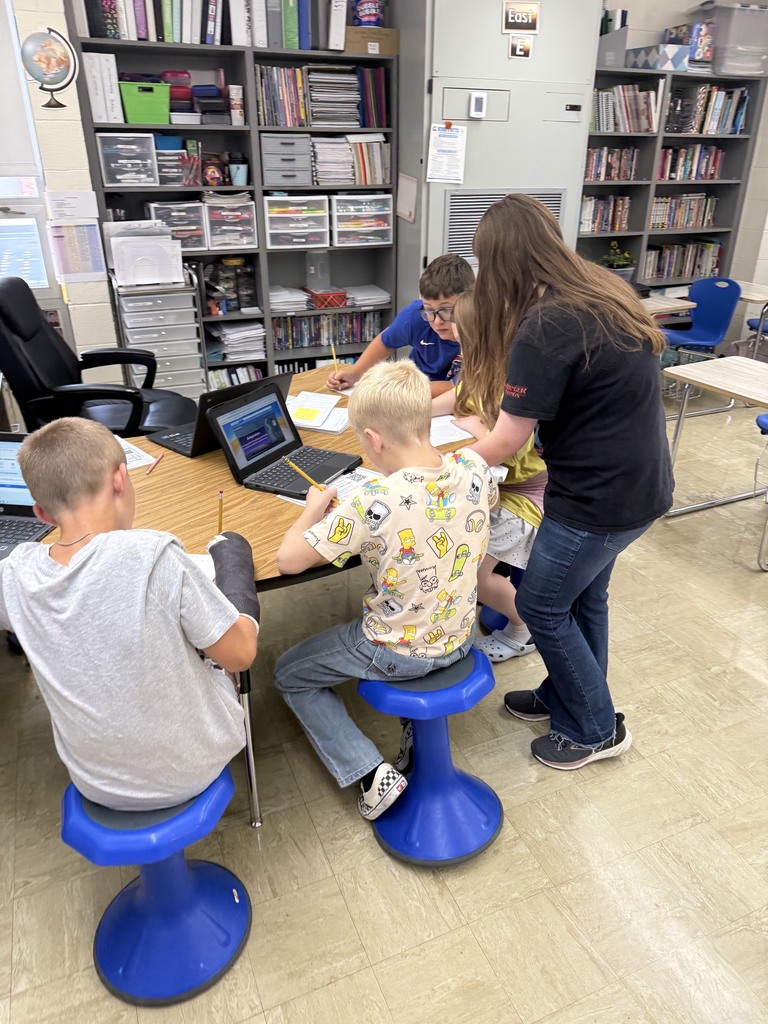 A group of five students is at an area of the room filling out a  packet together. 
