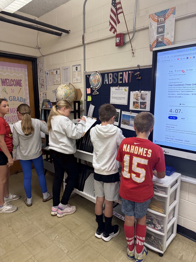 A group of five students is at an area of the room filling out a  packet together. 