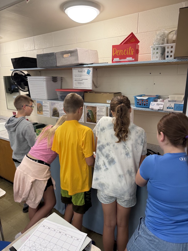 A group of five students is at an area of the room filling out a  packet together. 