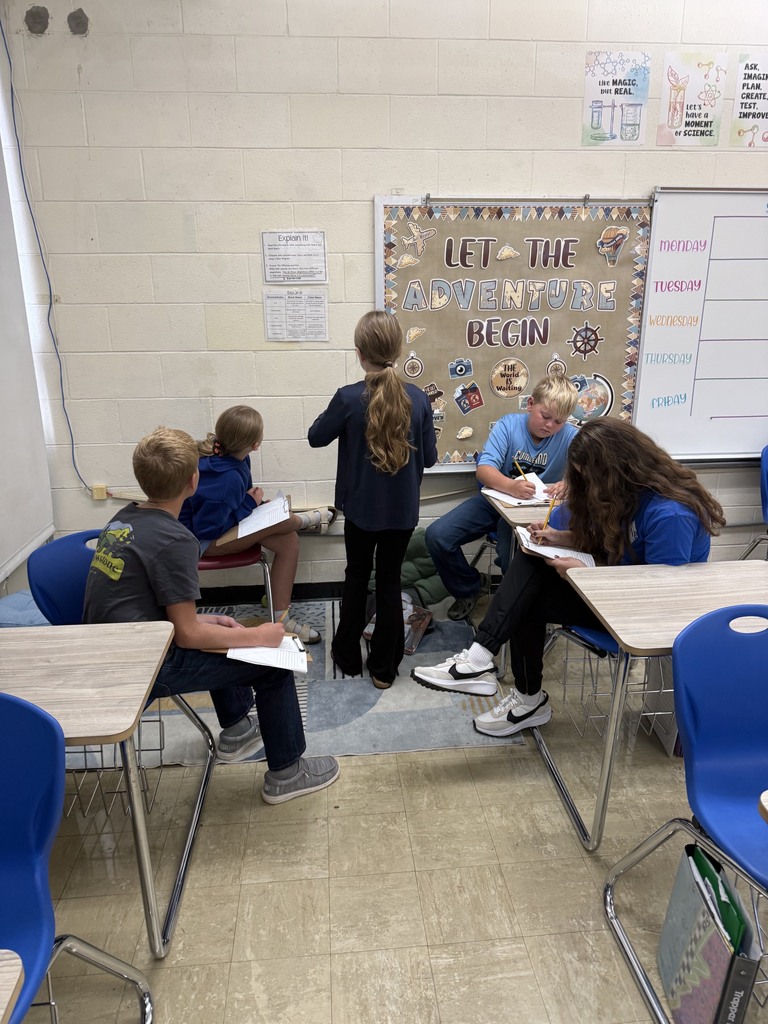A group of five students is at an area of the room filling out a  packet together. 