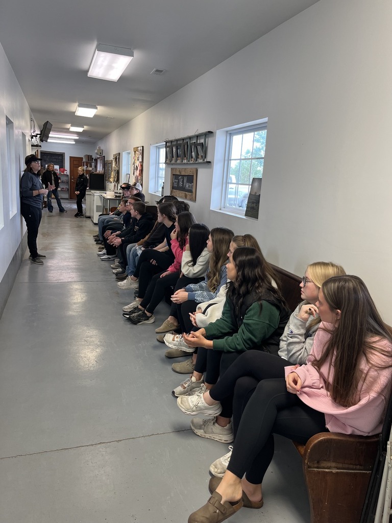 Students are sitting in the hallway of Marcoot's listening to a speaker.