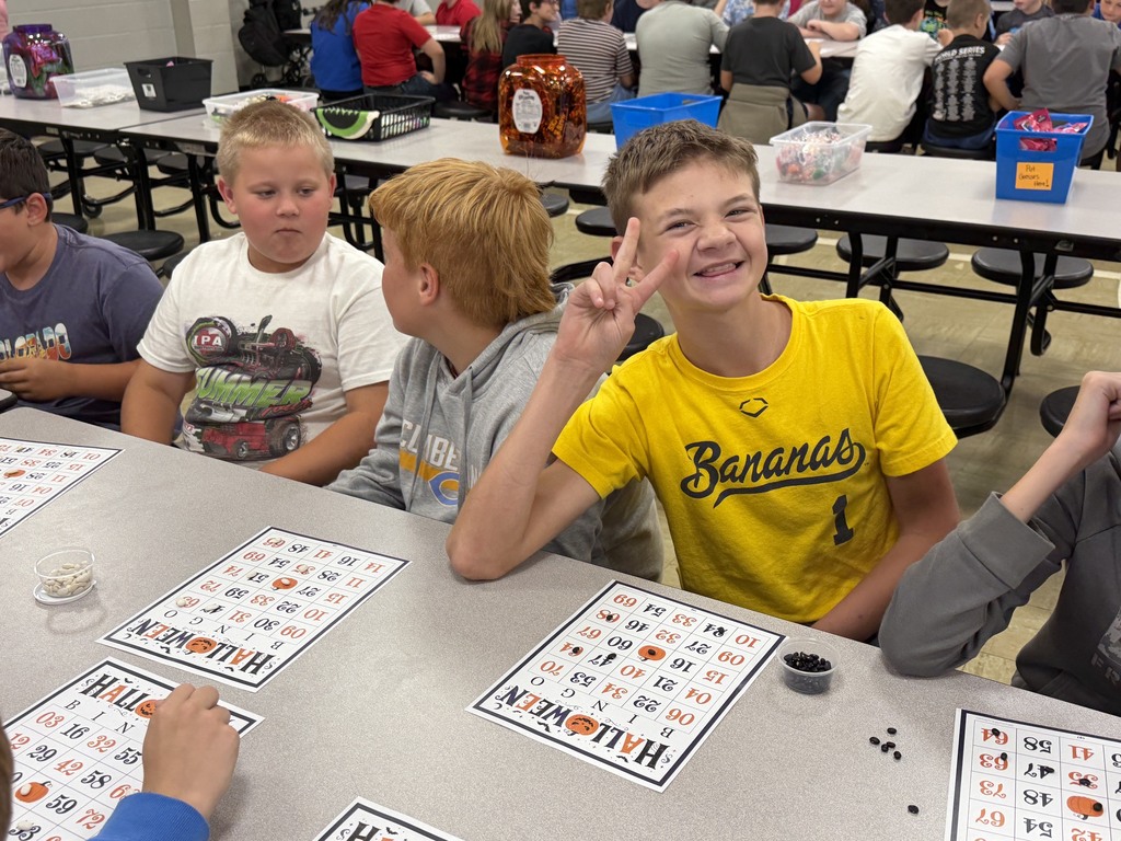 Three students are playing Bingo. One of them is smiling and giving the peace sign.