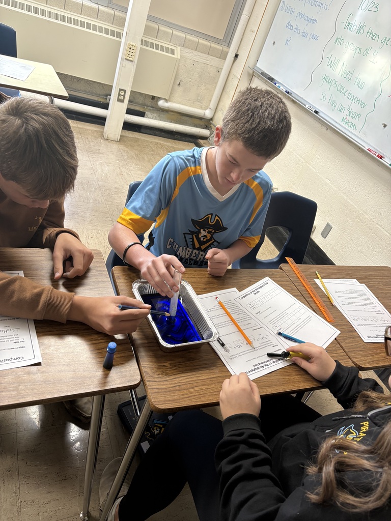 Three students are holding a test tube upside down in a pan of colored water watching the water rise into the tube.