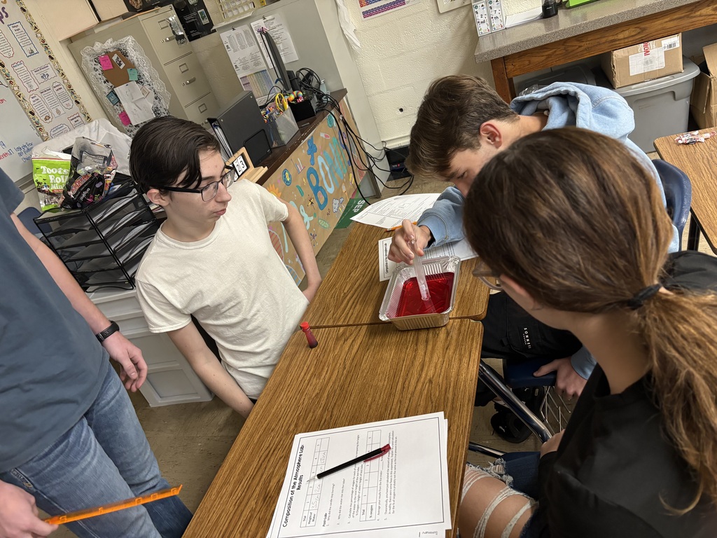 Four students are holding a test tube upside down in a pan of colored water watching the water rise into the tube.