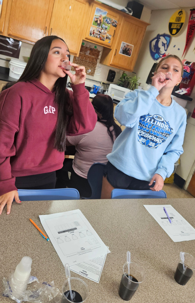 Two students are drinking a liquid to figure out the mystery flavor. 