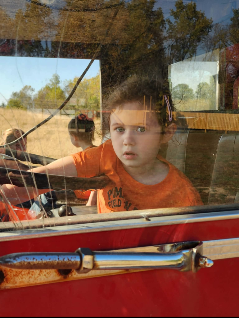 A student is sitting behind the wheel of a vehicle that is used for kids to explore. 