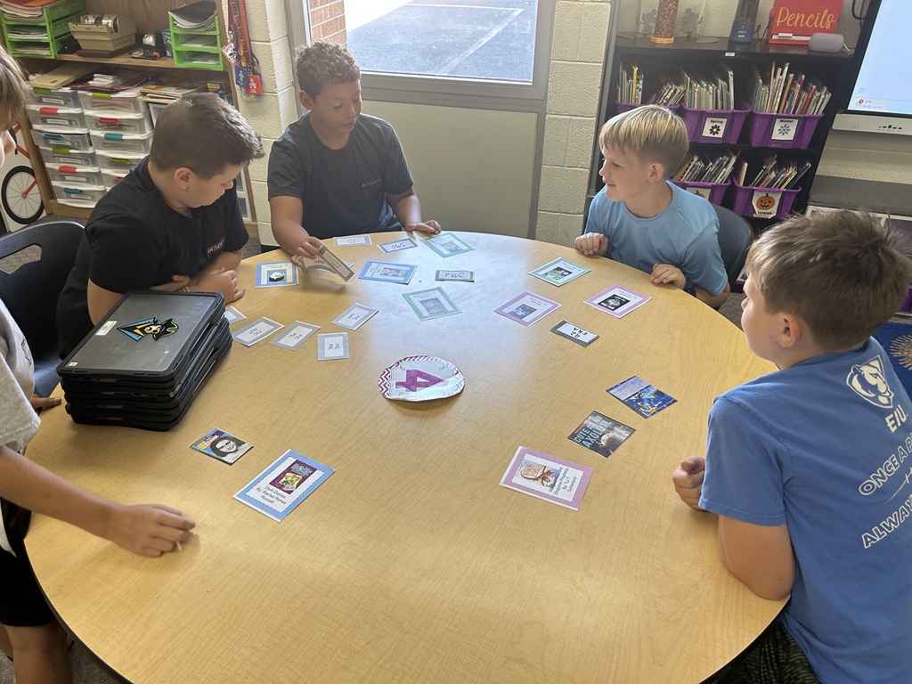Four students are sitting at a round table sorting cards for the library system.