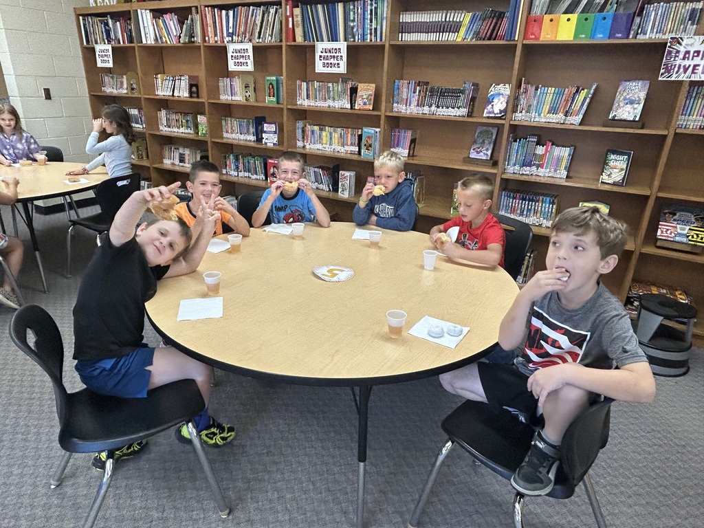Six students are sitting at a round tableeating their donut or driink their juice. 