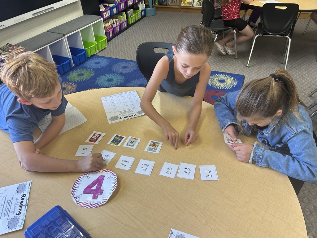 Three students are sitting at a round table sorting cards for the library system.