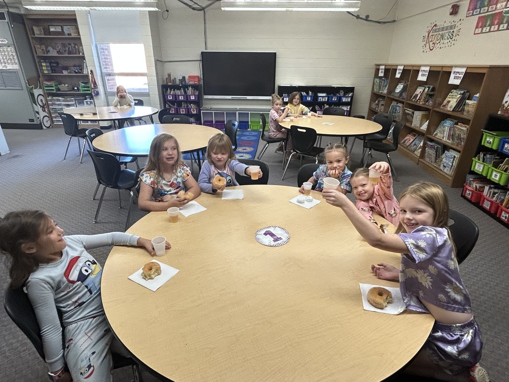 Six students are sitting at a round tableeating their donut or driink their juice. 