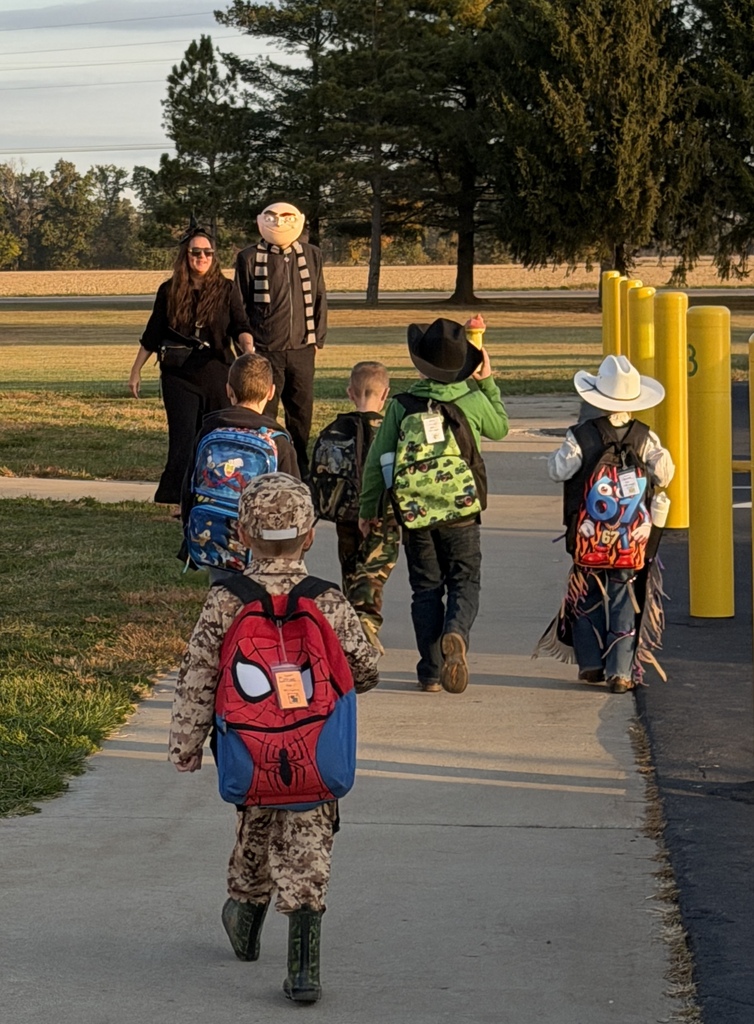 Five students are walking toward the two principals. The principals are dressed like a minions character and a witch.
