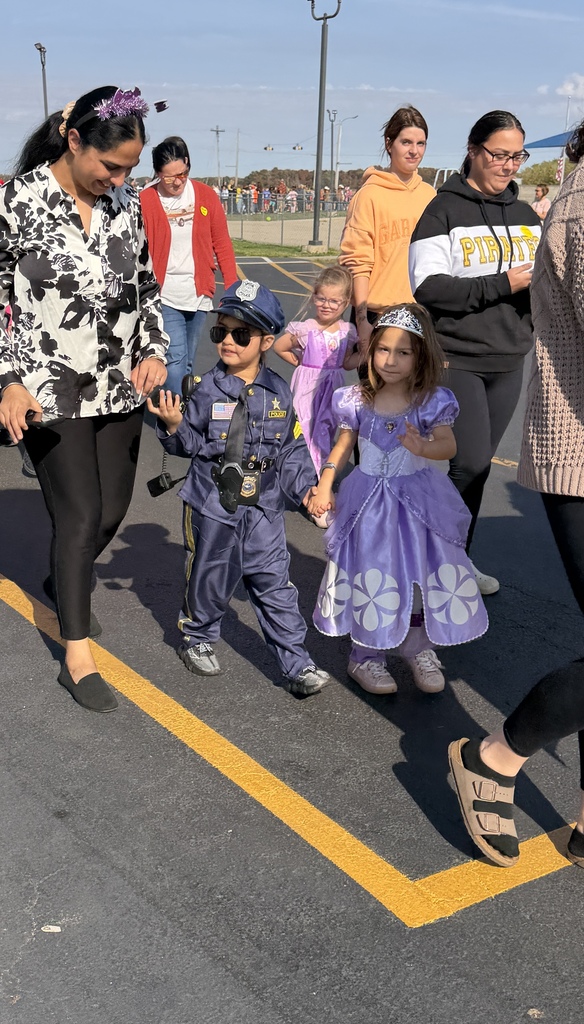 Students and parents are walking in the parade. One student is a princess in purple and the other is a police officer. 