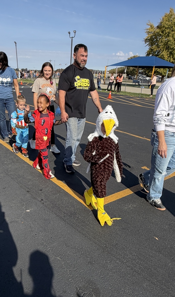 Students and parents are walking in the parade. One is an eagle. The other two students are animated characters. 