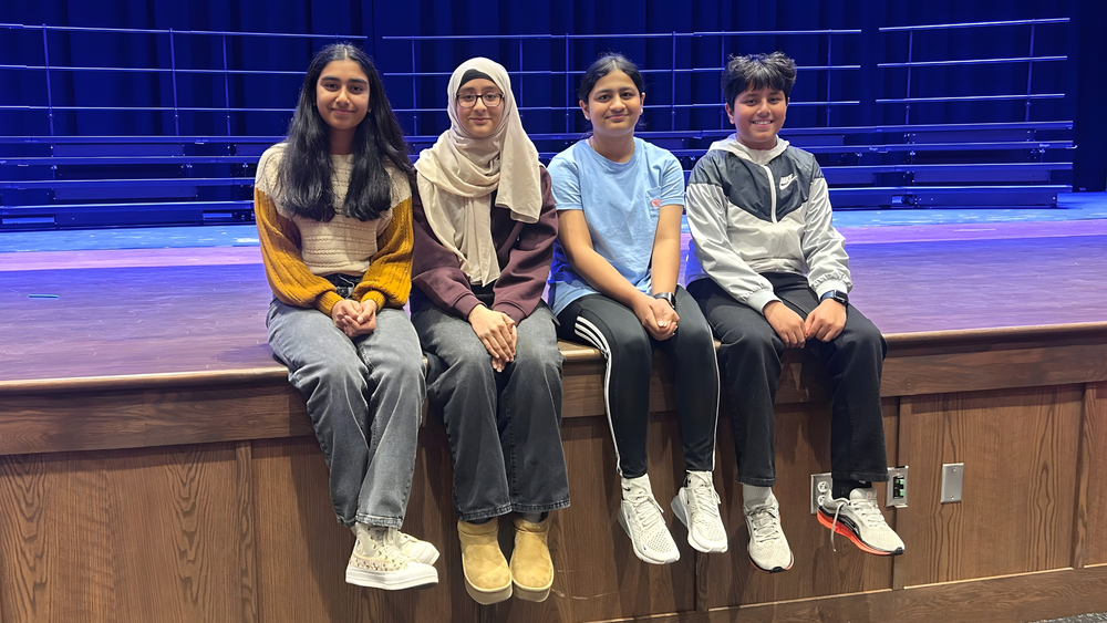 Four Eagle View Middle School students sit on the stage, posing for a picture to celebrate their success with moving on to the WITF Spelling Bee.