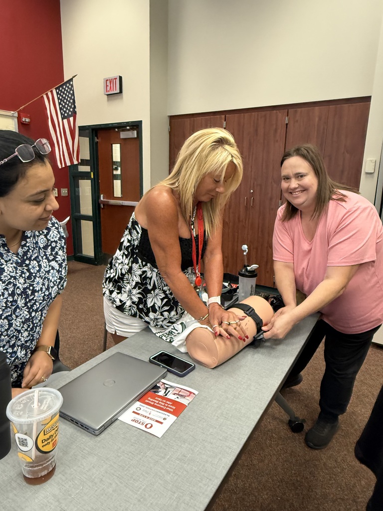 Three people practice wound packing on a training limb at a table.