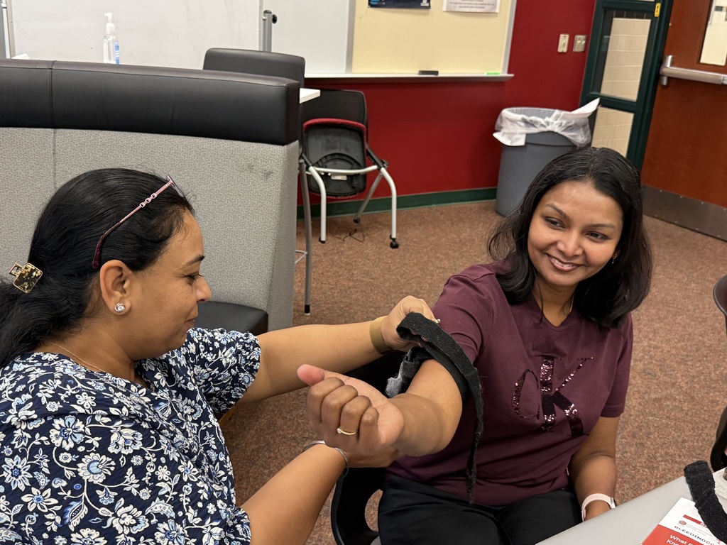 Person applies a tourniquet to another's arm in a room.