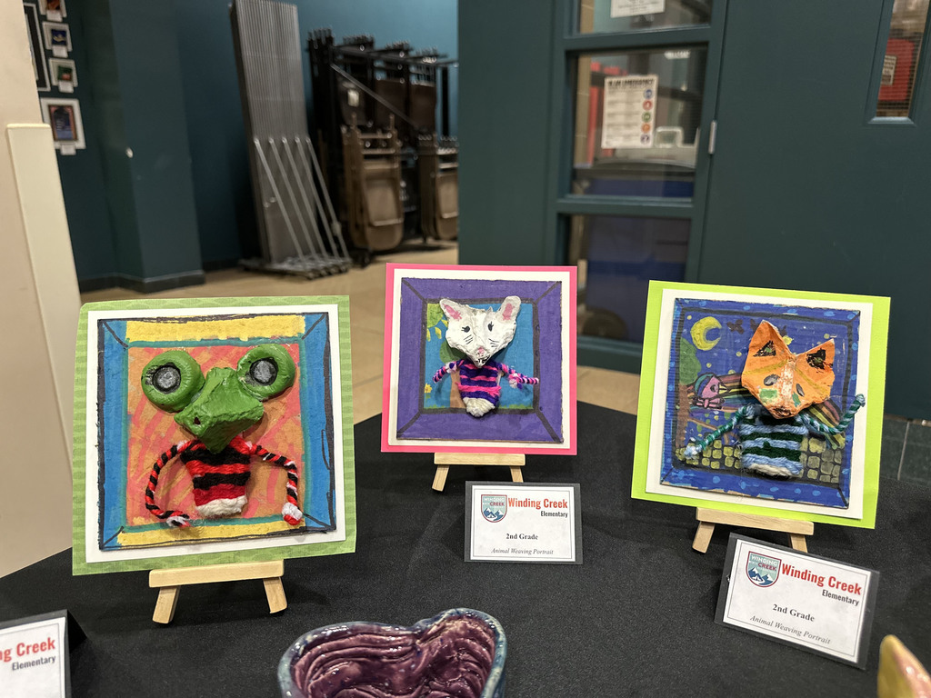 Three colorful 3D animal artworks by 2nd-grade students displayed on easels.