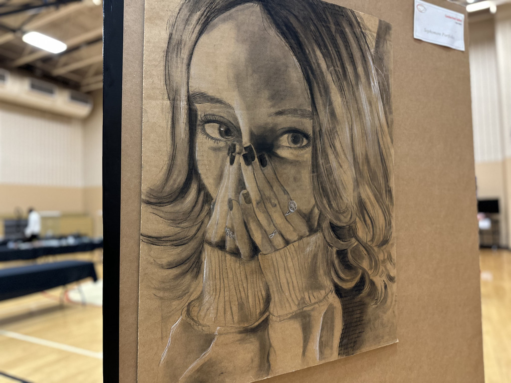 Charcoal drawing of a person with long, wavy hair on an easel in a gymnasium.