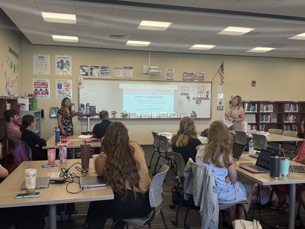 Classroom presentation with new CV staff attendees seated at tables and two women presenting at the front.