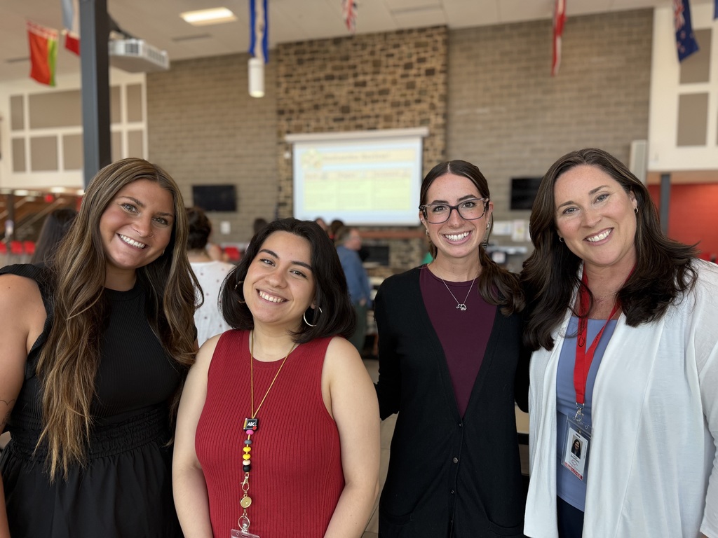 Four new Cumberland Valley staff members standing in a room with flags and a projector screen in the background.
