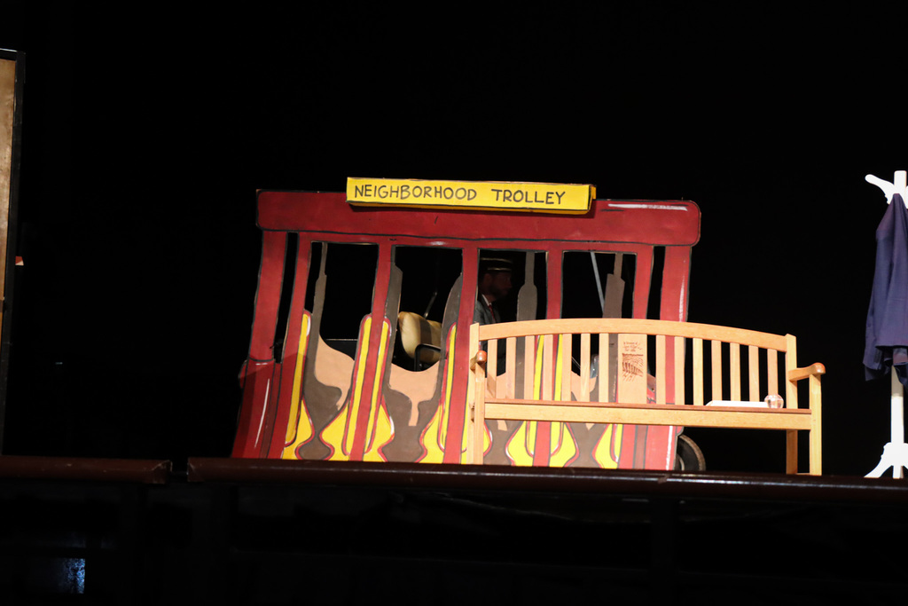 Stage set with a red and yellow 'Neighborhood Trolley' that drives across during the performance.
