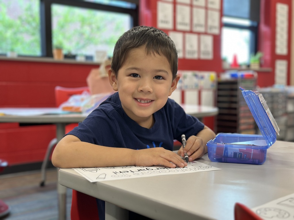 Kindergartener working on a coloring sheet at a desk on the first day of school.