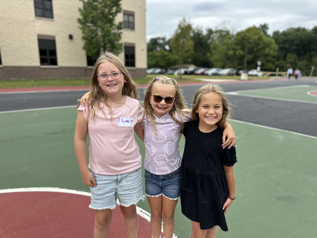 Three children with arms around each other on a school basketball court.
