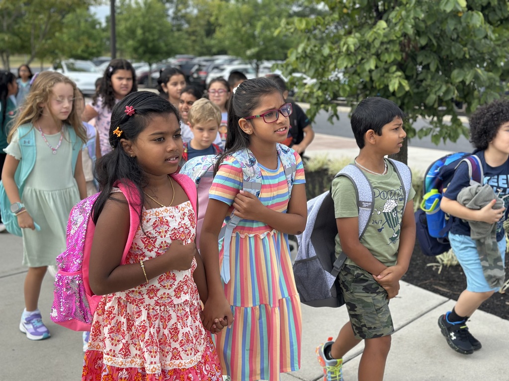Children with backpacks walking hand-in-hand on a sidewalk.