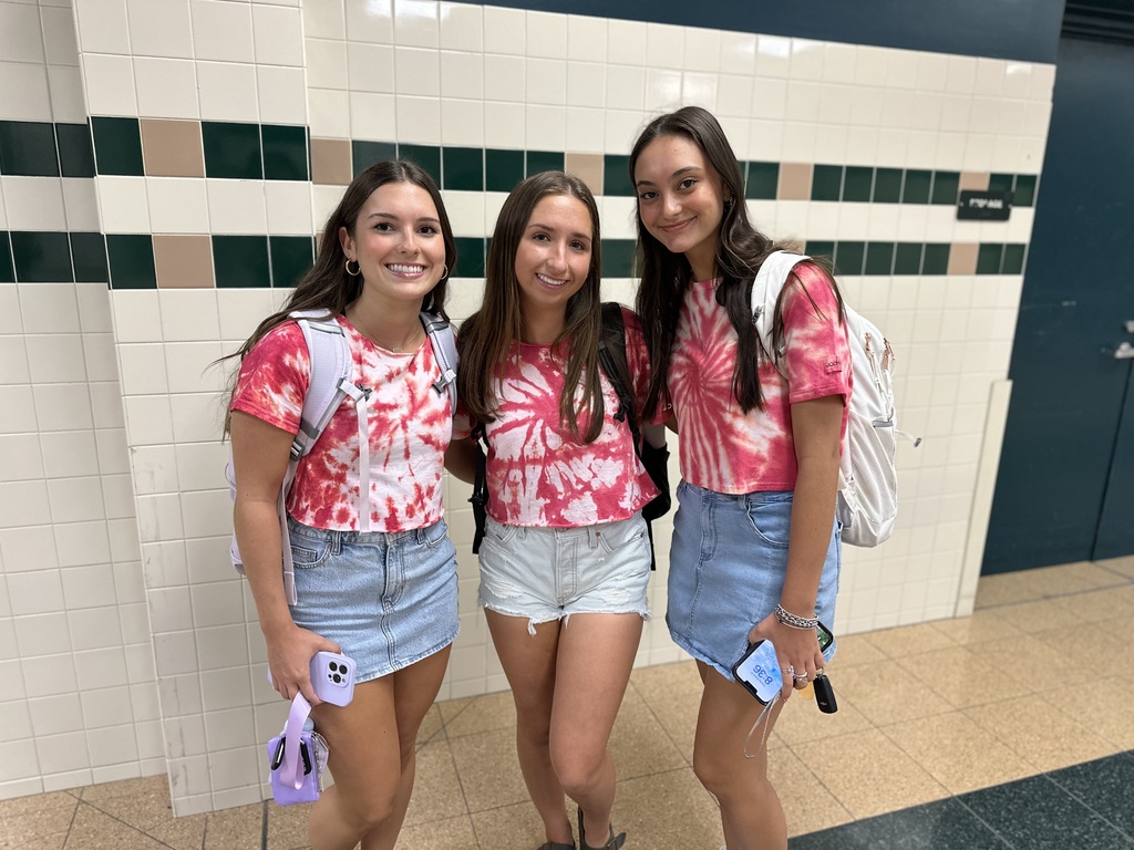 Three people in red and white tie-dye shirts with backpacks standing in a hallway.