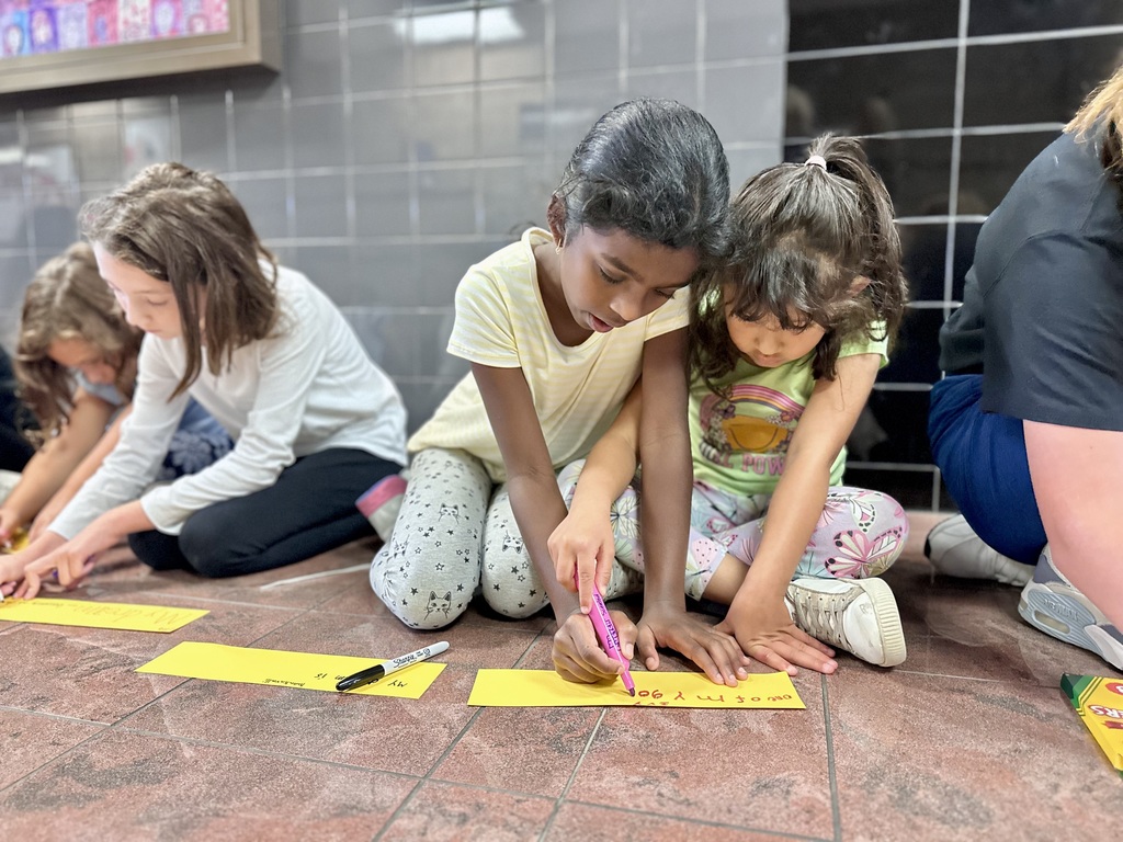 Children sitting on the floor at the Star Lab Planetarium, writing on yellow paper strips.
