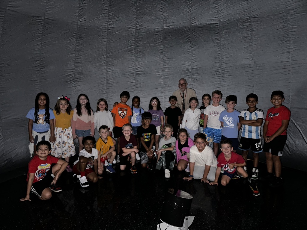 Children and an adult pose inside the Star Lab Planetarium in front of a large gray dome.