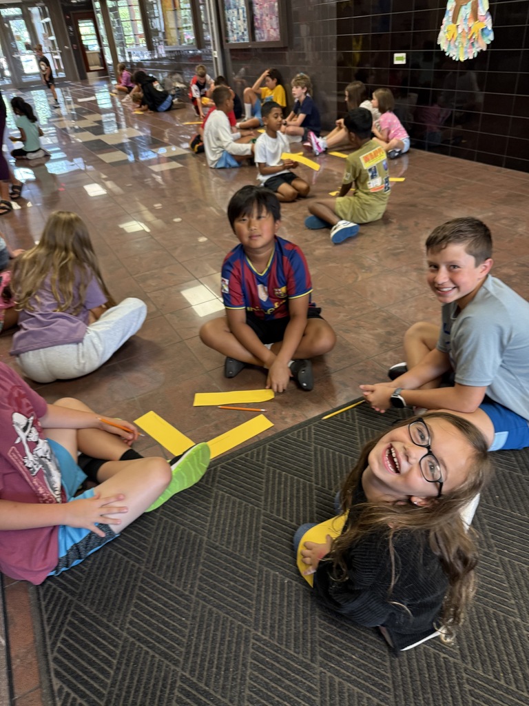 Children seated in groups on the floor, working with yellow paper strips for a group activity about the Star Lab Planetarium.