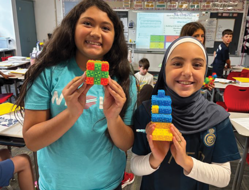 Two students in a classroom holding colorful interlocking block structures.