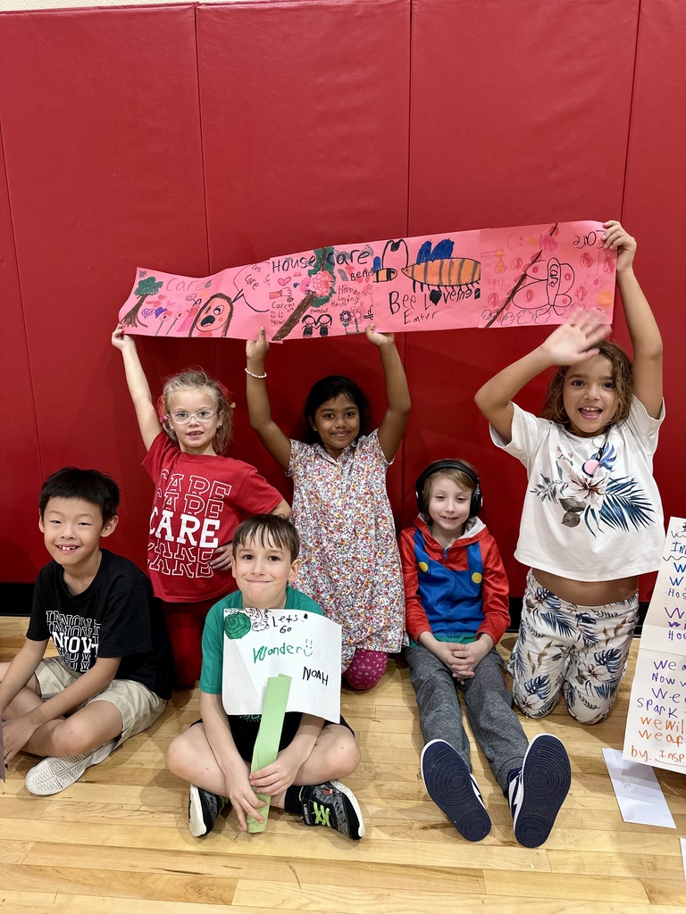 Five children in front of a red wall displaying colorful signs promoting kindness.
