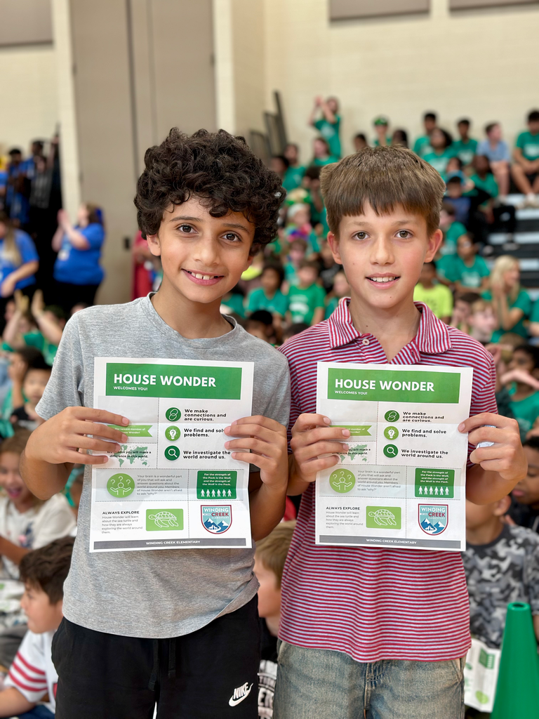 Two students in a gym holding signs for their new school house, 'House Wonder'.