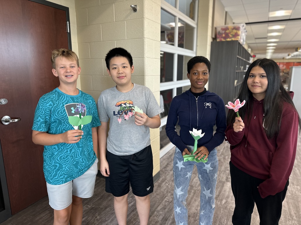 Four students in a hallway holding paper flower crafts.
