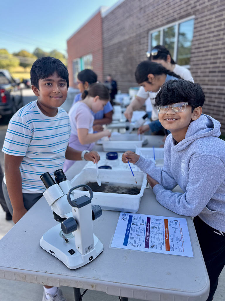 Children gathered around tables for an outdoor science activity with microscopes and materials.